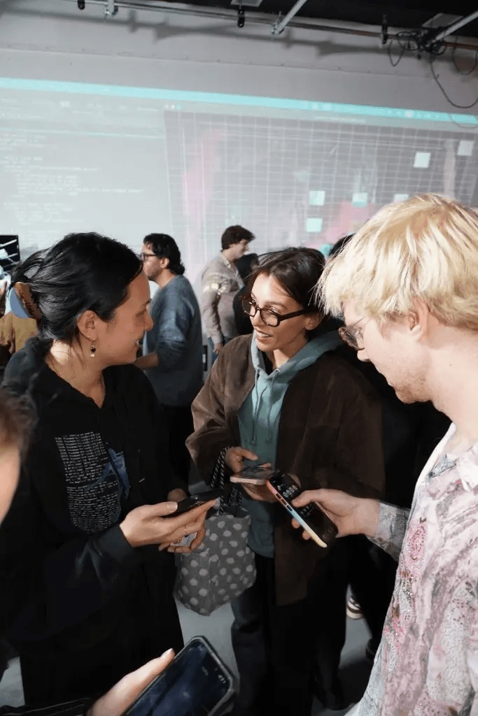 Three people comparing phones, code and UI projected on the wall behind them.