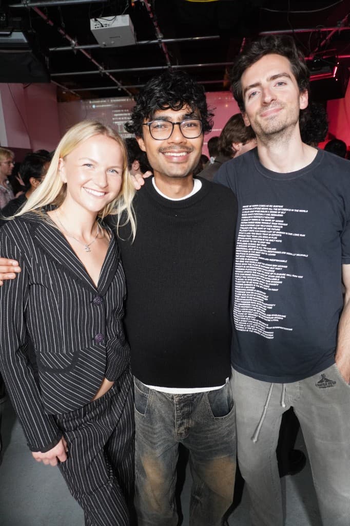 Three people smiling together, projector and screen visible behind.